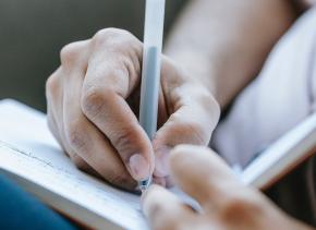 Close-up of writer's hands holding a pen and notebook