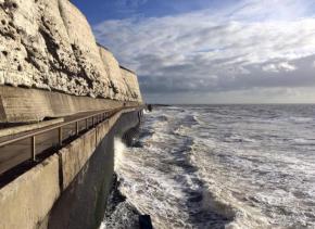 This image shows the sea crashing against the wall. To the left, is the path I walk along every day, and above that are the chalk cliffs. The sky is a mixture of cloud and blue.